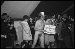 Yippies on stage at the Counter-inaugural Ball, 1969: naked man in an Uncle Sam hat holds a sign reading 'Self-determination for Vietnam'