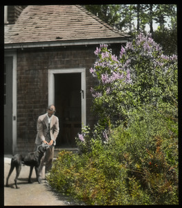 Lilacs Mr. Churchill (Man with dog in front of wooden building near lilacs)