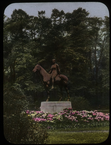 Statue of woman on horseback surrounded by planting of rhododendron, trees in background