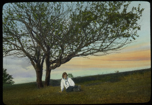 Girl sitting under fruit tree on hillside in spring