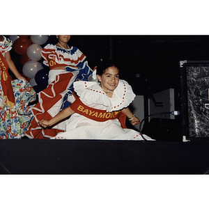 A girl kneels on stage wearing a Bayamon sash at the Festival Puertorriqueño