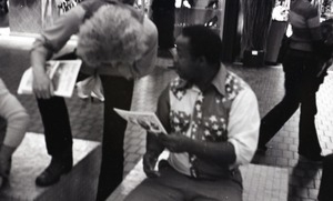 Commune member distributing Free Spirit Press in an indoor shopping mall: communard looking over shoulder of African American man