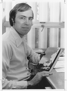 Richard E. Webb seated at his desk holding his newly published book
