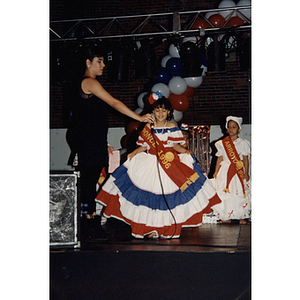 A girl in a red, white, and blue dress speaks into a microphone at the Festival Puertorriqueño