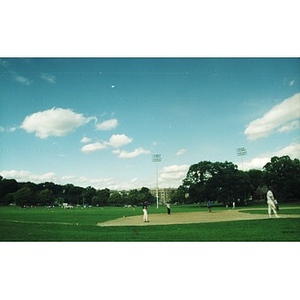 Baseball game being played in a large park under a blue sky.
