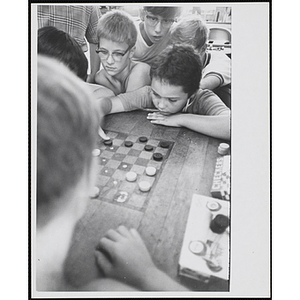 As a group of boys look on, two boys play checkers