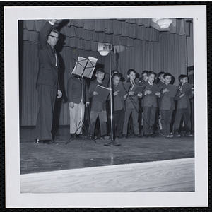 A man conducts a boys' choir on a stage at a Christmas party