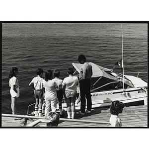 A Group of children and an adult standing on a dock next to a motorboat