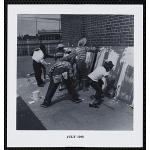 A group of boys paint on large pieces of plywood propped against a brick wall