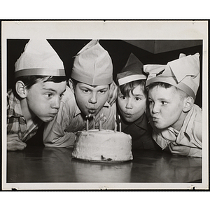 Four boys blow out candles on a cake