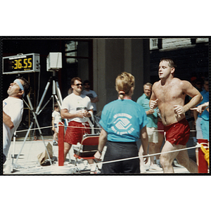 A man runs across the finish line as a race official looks on during the Battle of Bunker Hill Road Race