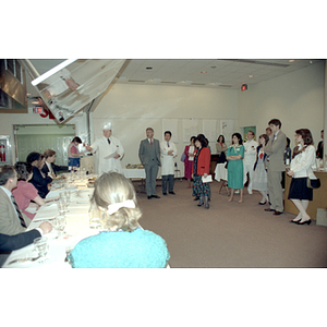 Chef addresses standing onlookers and sitting judges at a food tasting event