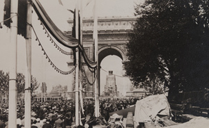 View of crowds gathered under the Arc de Triomphe, bleachers set up and poles strung with banners, Paris, July 13, 1919