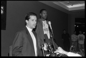 John Calipari at the microphone during a press conference with Marcus Camby (background)