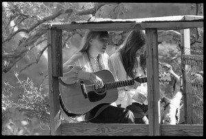 Joni Mitchell with guitar, seated in her tree house in Laurel Canyon with Judy Collins: close-up