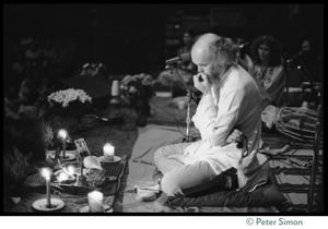 Ram Dass seated onstage at the Winterland Ballroom during his 'marathon,' head bowed