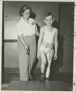 A physical therapist helps a young boy practice walking with his prosthetic leg