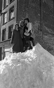 Three women posing atop large snowpile