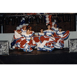 Seven girls dance on stage in Puerto Rican flag dresses at the Festival Puertorriqueño