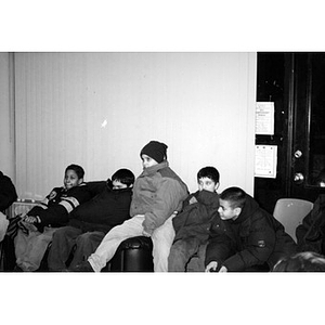 Group of boys in winter coats sitting together inside.