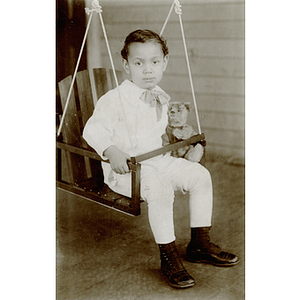 Charles Bruce Jr. holding a teddy bear, seated on a swing