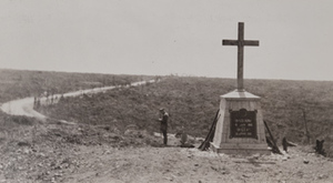 Rifles leaning against a large monument of a cross guarded by soldier, with fields and road in the background, Bayonet Trench, Verdun