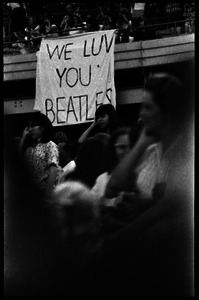 Beatles concert at Shea Stadium: fans standing beneath a banner reading 'We luv you Beatles,' hung on the overhang of the upper deck