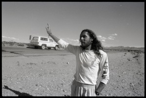 Peace encampment activist waving at a passing vehicle on the road near the entrance to the Nevada Test Site