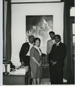 Shirley Graham Du Bois standing in front of W. E. B. Du Bois portrait with three unidentified men