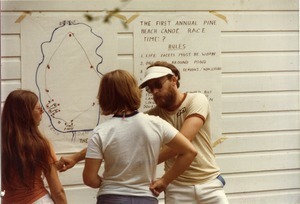 Man and women talking in front of a sign announcing the First Annual Pine Beach canoe race