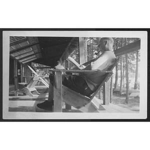 Man seated in chair and reading and smoking pipe