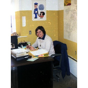 Female employee smiling, sitting behind a desk in an office at La Alianza Hispana, Roxbury, Mass.