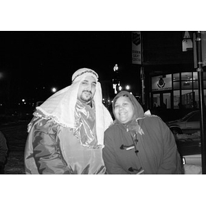 Man dressed as a Magi or shepherd poses outside in the cold with a woman bundled up in a coat and hood.