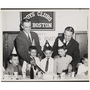 William J. Lynch pours a drink into a cup while an unidentified man cuts a cake for a group of boys in party hats