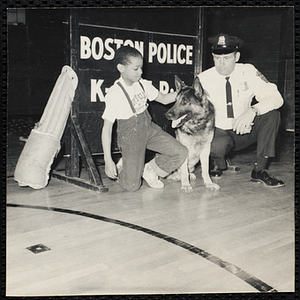 A boy posing with a police officer and K-9 dog during the K-9 demonstration by the Boston Police Department at the Boys' Clubs of Boston Roxbury Clubhouse