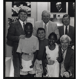 Two boys and a girl pose with four men, one of them holding a certificate, at a Boys and Girls Club event