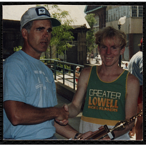 A runner receives a trophy and handshake from a man during the Battle of Bunker Hill Road Race