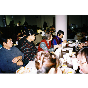 Chinese Progressive Association members sit at tables, eating Thanksgiving dinner