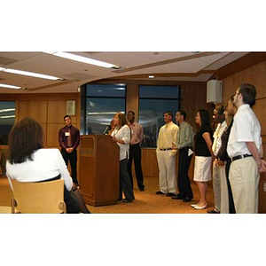 Nadia Alvarez speaks at a podium as the Torch Scholars stand behind her