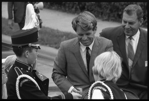 Robert F. Kennedy seated in an open car in a parade, shaking hands with the marching band while stumping for Democratic candidates in the northern Midwest