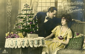 Postcard (colored) depicting man, woman, and Christmas tree reading 'Wesolych swiat bozego narodzenia'