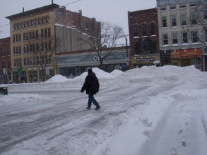 Man crossing Gothic Street, Northampton, Mass., at intersection with Main Street, amid deep piles of plowed snow