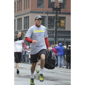 A male "One Run" runner in a "Boston Stands As One" Adidas t-shirt carries his bookbag and runs down Boylston Street