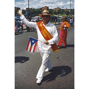 A man wears a sash and holds a Puerto Rican flag during the parade