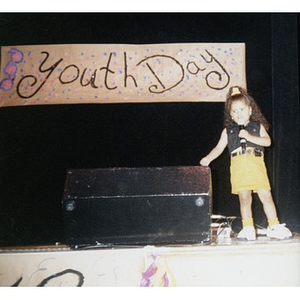 Little girl with a microphone on stage during an event called "Youth Day."