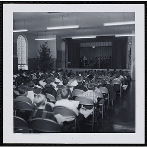 An audience of boys watches a boys' choir perform on stage