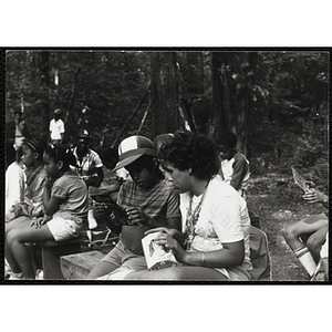 Two seated children examine each other's toys at a camp