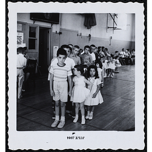 Boys hold hands with their sisters and stand in line in an auditorium at a Boys' Club Little Sister Contest