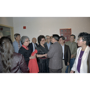 Member of the Consulate General of the People's Republic of China shakes hands with a woman surrounded by others at a welcome party held for the Consulate General's visit to Boston