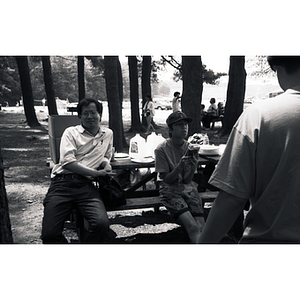 Man and a teenage boy sit at a table in a wooded picnic area